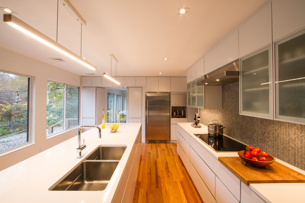 Bild på ett mellanstort funkis vit vitt kök, med en dubbel diskho, släta luckor, vita skåp, bänkskiva i kvartsit, grått stänkskydd, stänkskydd i stenkakel, rostfria vitvaror, ljust trägolv, en köksö och brunt golv