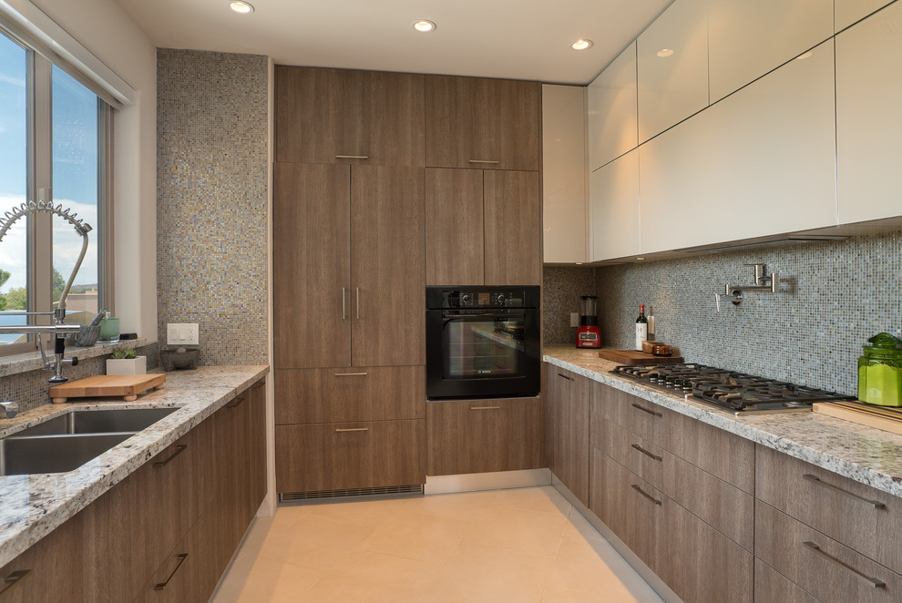 Cette image montre une grande cuisine design en U et bois brun avec un évier 2 bacs, un placard à porte plane, un électroménager noir, un plan de travail en granite, une crédence grise, une crédence en mosaïque et un sol beige.