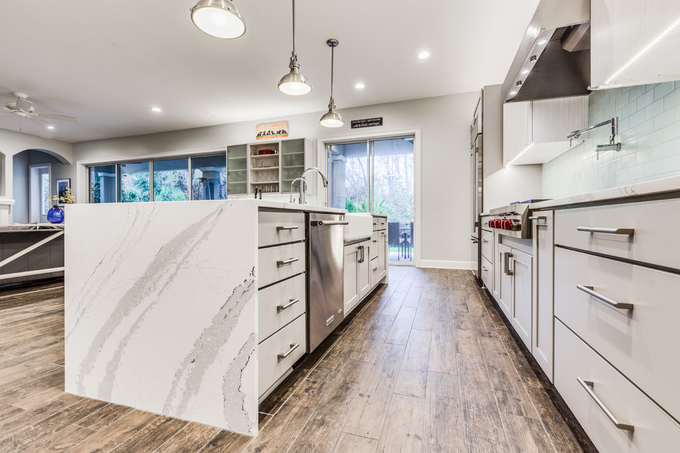 Eat-in kitchen - mid-sized transitional porcelain tile eat-in kitchen idea in Jacksonville with a farmhouse sink, flat-panel cabinets, gray cabinets, quartz countertops, green backsplash, glass tile backsplash, stainless steel appliances and an island