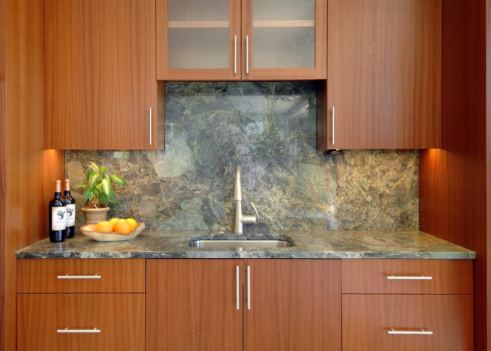 Bild på ett funkis linjärt kök, med släta luckor, skåp i mellenmörkt trä, granitbänkskiva, grönt stänkskydd, stänkskydd i sten och en undermonterad diskho