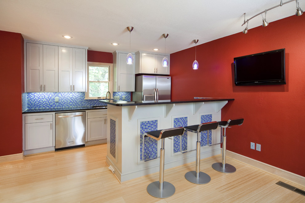Bild på ett funkis kök, med stänkskydd i mosaik, rostfria vitvaror, blått stänkskydd, luckor med infälld panel och vita skåp