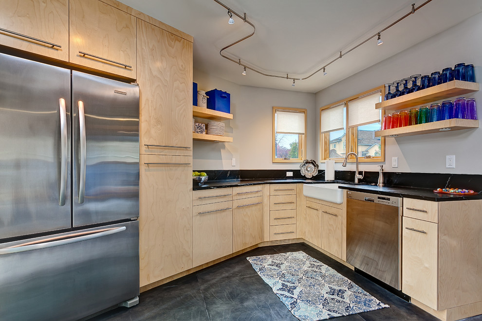 This is an example of a contemporary l-shaped kitchen in Boise with a belfast sink, flat-panel cabinets, light wood cabinets, soapstone worktops, black splashback, stainless steel appliances and concrete flooring.