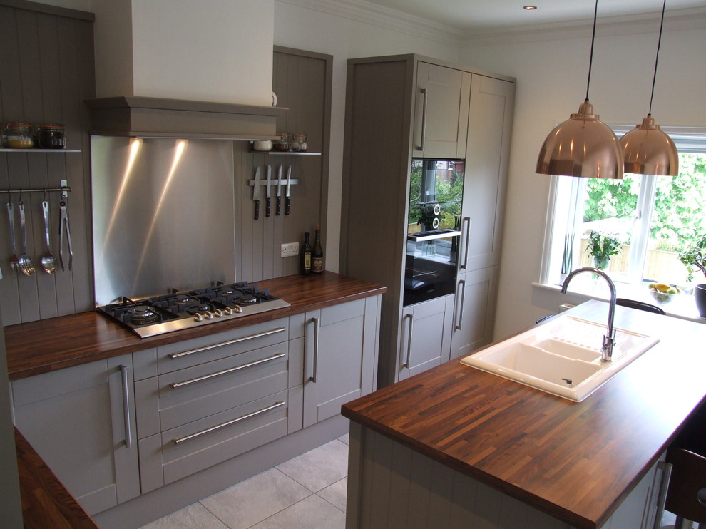 Medium sized romantic l-shaped open plan kitchen in Dorset with a built-in sink, shaker cabinets, grey cabinets, laminate countertops, grey splashback, black appliances, ceramic flooring and an island.