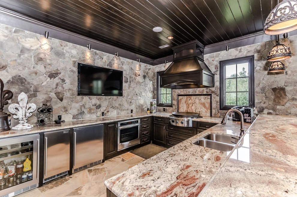 Foto på ett stort funkis kök, med en dubbel diskho, luckor med upphöjd panel, skåp i mörkt trä, granitbänkskiva, beige stänkskydd, stänkskydd i stenkakel, rostfria vitvaror, travertin golv och en halv köksö