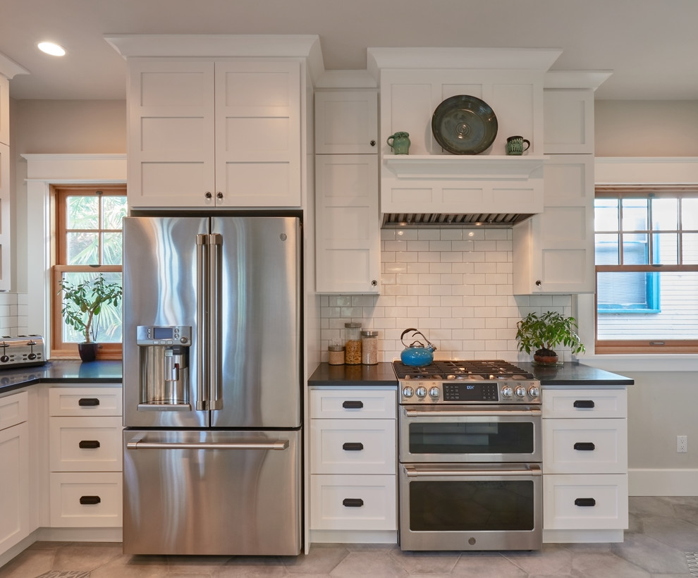 Mid-sized farmhouse u-shaped porcelain tile and gray floor eat-in kitchen photo in Seattle with a double-bowl sink, shaker cabinets, white cabinets, granite countertops, white backsplash, subway tile backsplash, stainless steel appliances, a peninsula and black countertops