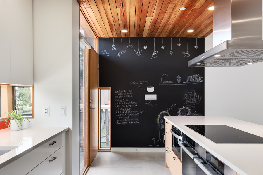 Moderne Küche in L-Form mit Unterbauwaschbecken, flächenbündigen Schrankfronten, weißen Schränken, Quarzwerkstein-Arbeitsplatte, Küchenrückwand in Orange, Glasrückwand, Küchengeräten aus Edelstahl, Betonboden und Kücheninsel in Vancouver