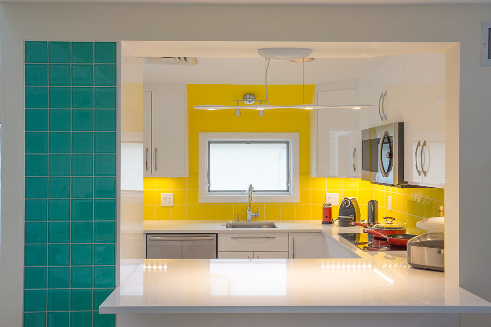 Foto på ett funkis kök, med gult stänkskydd, stänkskydd i keramik, en undermonterad diskho, släta luckor, vita skåp och rostfria vitvaror