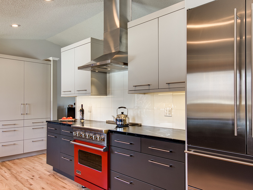 Inspiration for a mid-sized contemporary galley light wood floor kitchen remodel in Denver with an undermount sink, flat-panel cabinets, gray cabinets, soapstone countertops, white backsplash, glass tile backsplash and stainless steel appliances