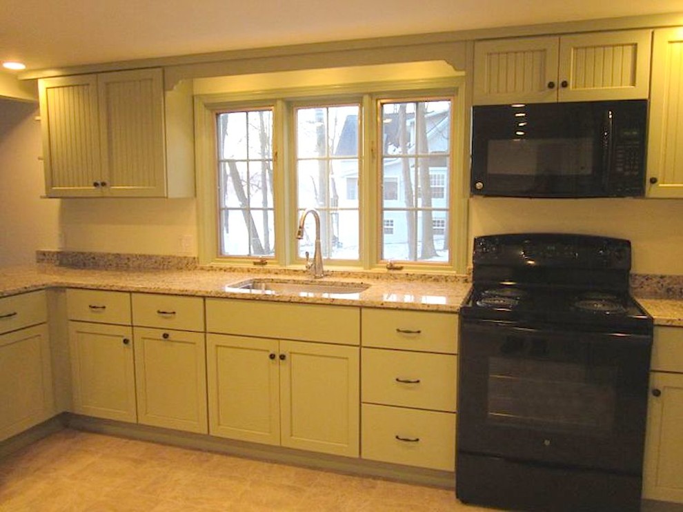 Lantlig inredning av ett mellanstort kök, med en undermonterad diskho, släta luckor, gröna skåp, granitbänkskiva, svarta vitvaror, vinylgolv och en halv köksö
