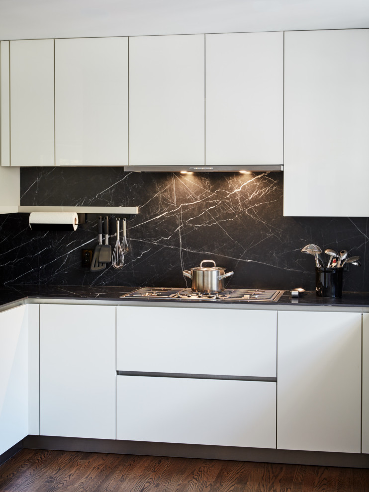 Immagine di una grande cucina minimalista con lavello sottopiano, ante di vetro, ante bianche, paraspruzzi nero, elettrodomestici in acciaio inossidabile, parquet scuro, pavimento marrone e top nero