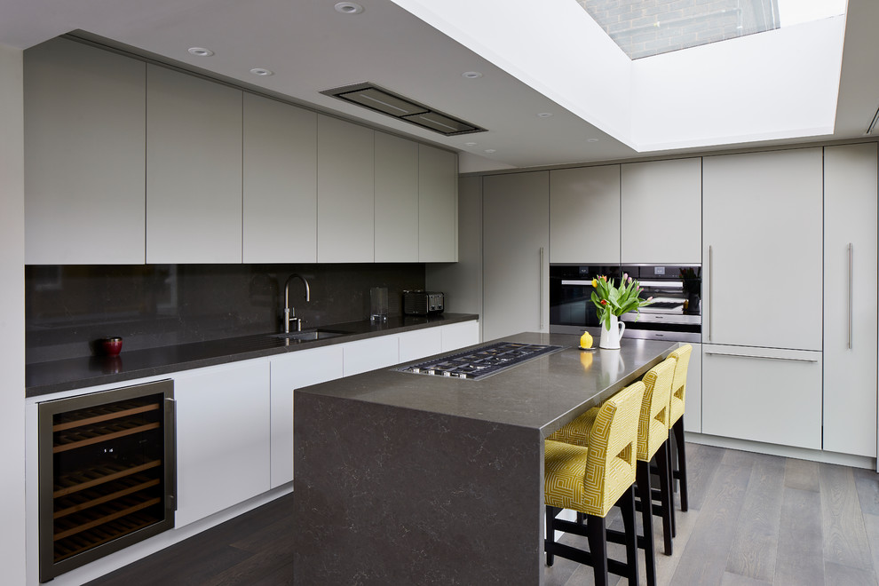 This is an example of a medium sized contemporary u-shaped kitchen in London with flat-panel cabinets, grey cabinets, marble worktops, grey splashback, marble splashback, light hardwood flooring, an island, grey floors, grey worktops, a submerged sink and black appliances.