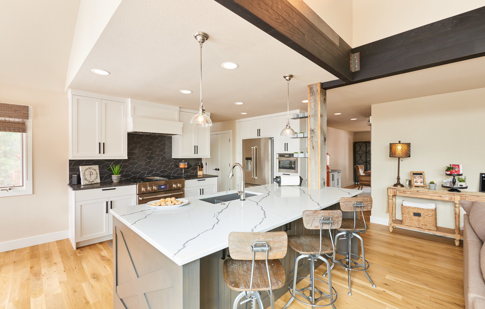 Example of a large transitional l-shaped light wood floor and brown floor open concept kitchen design in Denver with an undermount sink, shaker cabinets, white cabinets, quartz countertops, black backsplash, ceramic backsplash, stainless steel appliances, an island and white countertops