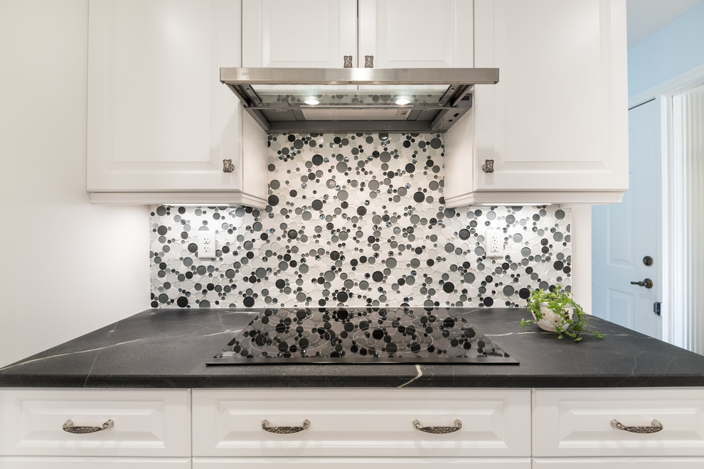 Exempel på ett klassiskt kök, med en enkel diskho, luckor med upphöjd panel, vita skåp, bänkskiva i täljsten, vitt stänkskydd, stänkskydd i glaskakel och svarta vitvaror