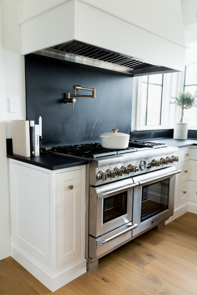 Inredning av ett klassiskt stort svart svart kök, med en undermonterad diskho, luckor med infälld panel, vita skåp, bänkskiva i kalksten, svart stänkskydd, stänkskydd i kalk, rostfria vitvaror, ljust trägolv, en köksö och brunt golv