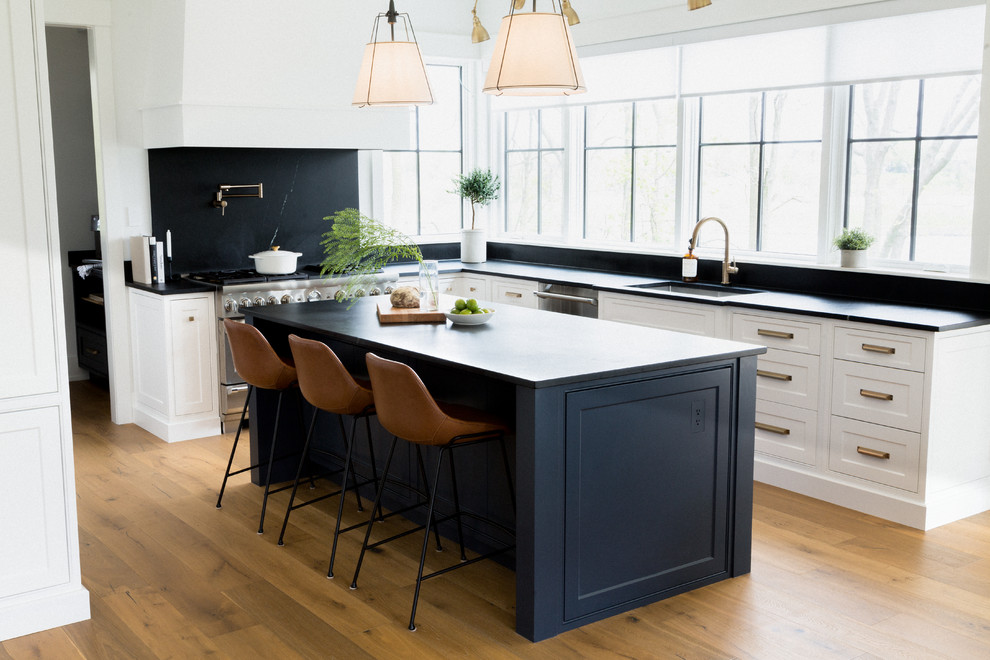 Inspiration for a large transitional u-shaped light wood floor and brown floor open concept kitchen remodel in Toronto with an undermount sink, recessed-panel cabinets, white cabinets, limestone countertops, black backsplash, limestone backsplash, stainless steel appliances, an island and black countertops