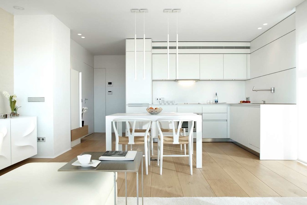 Стильный дизайн: угловая кухня-гостиная среднего размера в современном стиле с плоскими фасадами, белыми фасадами, белым фартуком, светлым паркетным полом и техникой из нержавеющей стали без острова - последний тренд