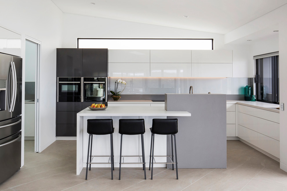 Moderne Küche in U-Form mit flächenbündigen Schrankfronten, weißen Schränken, Küchenrückwand in Weiß, Glasrückwand, Küchengeräten aus Edelstahl, Kücheninsel, beigem Boden und weißer Arbeitsplatte in Sydney