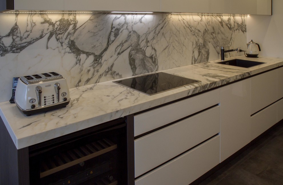 Foto di una piccola cucina parallela minimalista chiusa con ante lisce, ante bianche, top in marmo, paraspruzzi in lastra di pietra e nessuna isola