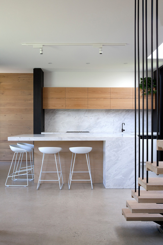 Réalisation d'une cuisine parallèle minimaliste en bois brun avec un placard à porte plane, une crédence blanche, sol en béton ciré, îlot, un sol gris et un plan de travail blanc.