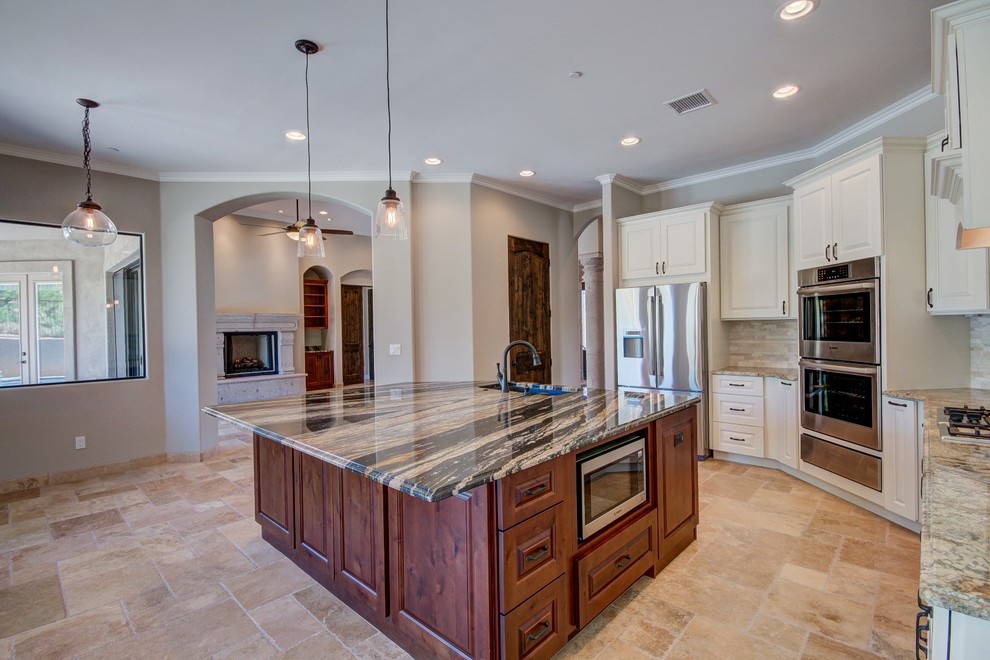 Foto på ett medelhavsstil kök, med en nedsänkt diskho, luckor med upphöjd panel, vita skåp, granitbänkskiva, beige stänkskydd, stänkskydd i stenkakel, rostfria vitvaror, travertin golv och en köksö