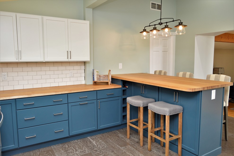 Inspiration for a mid-sized coastal u-shaped laminate floor and brown floor open concept kitchen remodel in Chicago with a farmhouse sink, shaker cabinets, blue cabinets, wood countertops, white backsplash, subway tile backsplash, stainless steel appliances, a peninsula and brown countertops