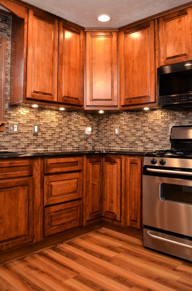 Inredning av ett klassiskt mellanstort svart svart kök, med en undermonterad diskho, luckor med upphöjd panel, skåp i mellenmörkt trä, granitbänkskiva, flerfärgad stänkskydd, stänkskydd i stickkakel, rostfria vitvaror, mellanmörkt trägolv, en halv köksö och brunt golv