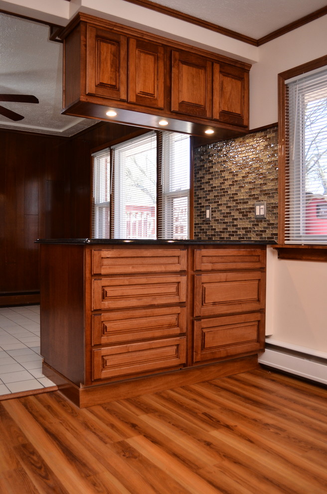 Example of a mid-sized classic l-shaped medium tone wood floor and brown floor eat-in kitchen design in Other with an undermount sink, raised-panel cabinets, medium tone wood cabinets, granite countertops, multicolored backsplash, matchstick tile backsplash, stainless steel appliances, a peninsula and black countertops