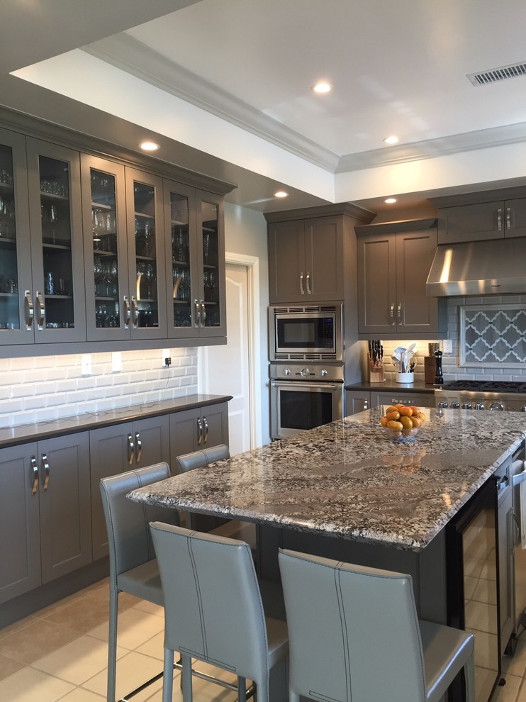 Photo of a large traditional u-shaped kitchen pantry in Los Angeles with a belfast sink, shaker cabinets, grey cabinets, granite worktops, beige splashback, ceramic splashback, stainless steel appliances, porcelain flooring and an island.