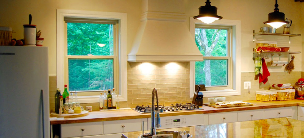モントリオールにある中くらいなカントリー風のおしゃれなキッチン (ドロップインシンク、フラットパネル扉のキャビネット、白いキャビネット、大理石カウンター、ベージュキッチンパネル、サブウェイタイルのキッチンパネル、白い調理設備) の写真
