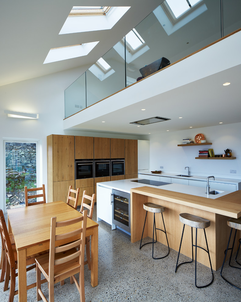 На фото: угловая кухня-гостиная в современном стиле с врезной мойкой, плоскими фасадами, светлыми деревянными фасадами, белым фартуком и островом