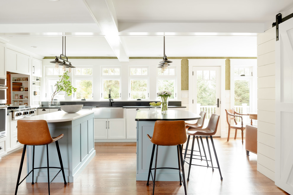 Mittelgroße Klassische Küche in L-Form mit Landhausspüle, Speckstein-Arbeitsplatte, zwei Kücheninseln, braunem Boden, Schrankfronten im Shaker-Stil, weißen Schränken, braunem Holzboden und schwarzer Arbeitsplatte in Boston