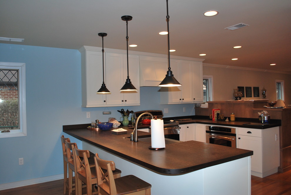 Modern inredning av ett litet kök, med luckor med infälld panel, vita skåp, bänkskiva i koppar, mellanmörkt trägolv och en halv köksö