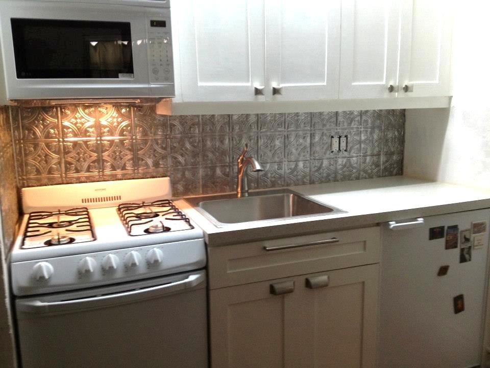 Bild på ett avskilt, litet funkis linjärt kök, med en nedsänkt diskho, skåp i shakerstil, vita skåp, laminatbänkskiva, stänkskydd med metallisk yta, vita vitvaror och mörkt trägolv