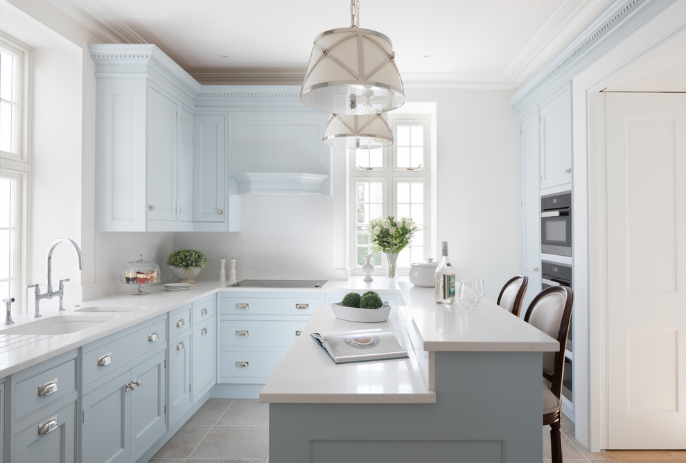 Inredning av ett klassiskt mellanstort vit vitt u-kök, med en undermonterad diskho, luckor med infälld panel, blå skåp, vitt stänkskydd, stänkskydd i sten, grått golv och en halv köksö