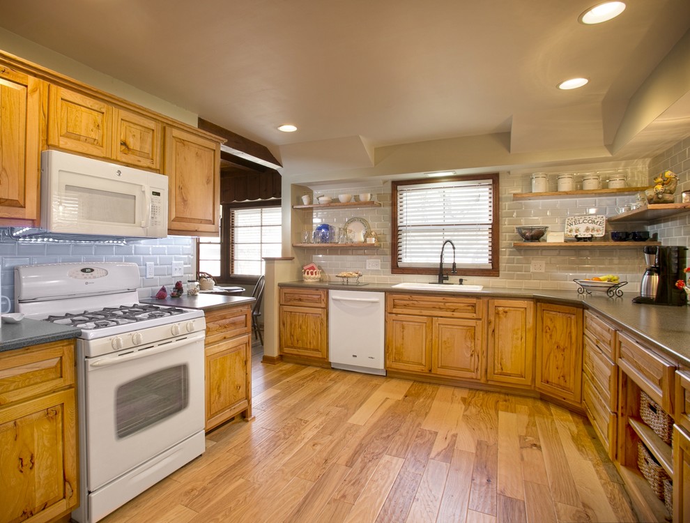Photo of a large country u-shaped enclosed kitchen in Wichita with a built-in sink, raised-panel cabinets, medium wood cabinets, composite countertops, grey splashback, glass tiled splashback, white appliances, medium hardwood flooring and no island.