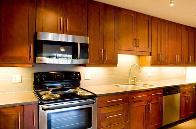 Foto på ett avskilt, mellanstort u-kök, med en nedsänkt diskho, luckor med infälld panel, skåp i mellenmörkt trä, laminatbänkskiva, grått stänkskydd, stänkskydd i sten, rostfria vitvaror och en köksö