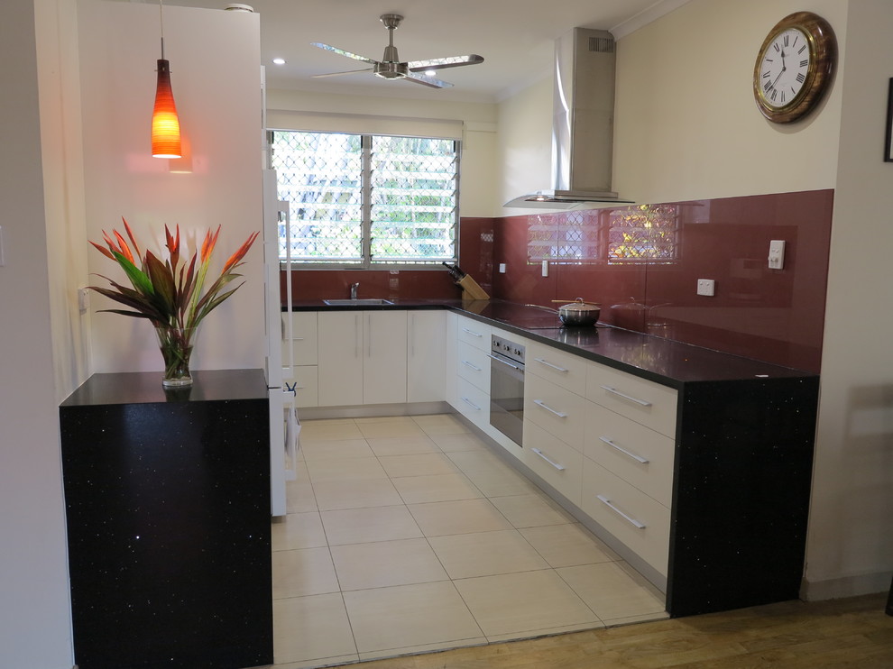 This is an example of a small world-inspired u-shaped kitchen pantry in Darwin with a single-bowl sink, white cabinets, engineered stone countertops, red splashback, stainless steel appliances and no island.