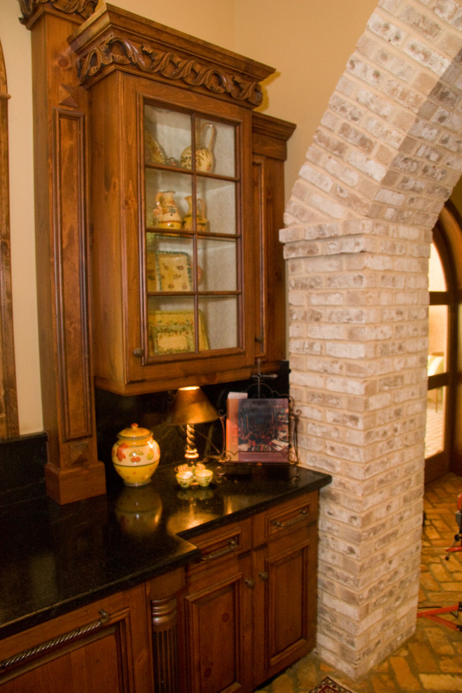 オーランドにある高級な中くらいなラスティックスタイルのおしゃれなキッチン (ガラス扉のキャビネット、中間色木目調キャビネット、御影石カウンター、黒いキッチンパネル、石スラブのキッチンパネル、レンガの床、アイランドなし) の写真