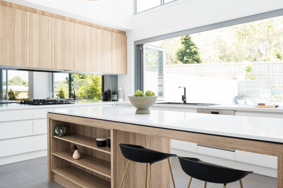 Moderne Küche in L-Form mit Einbauwaschbecken, flächenbündigen Schrankfronten, weißen Schränken, Rückwand-Fenster, Küchengeräten aus Edelstahl, Kücheninsel und grauem Boden in Brisbane
