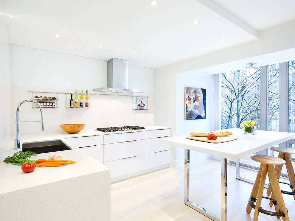 Bild på ett funkis l-kök, med en undermonterad diskho, släta luckor, vita skåp, vitt stänkskydd, ljust trägolv och en köksö