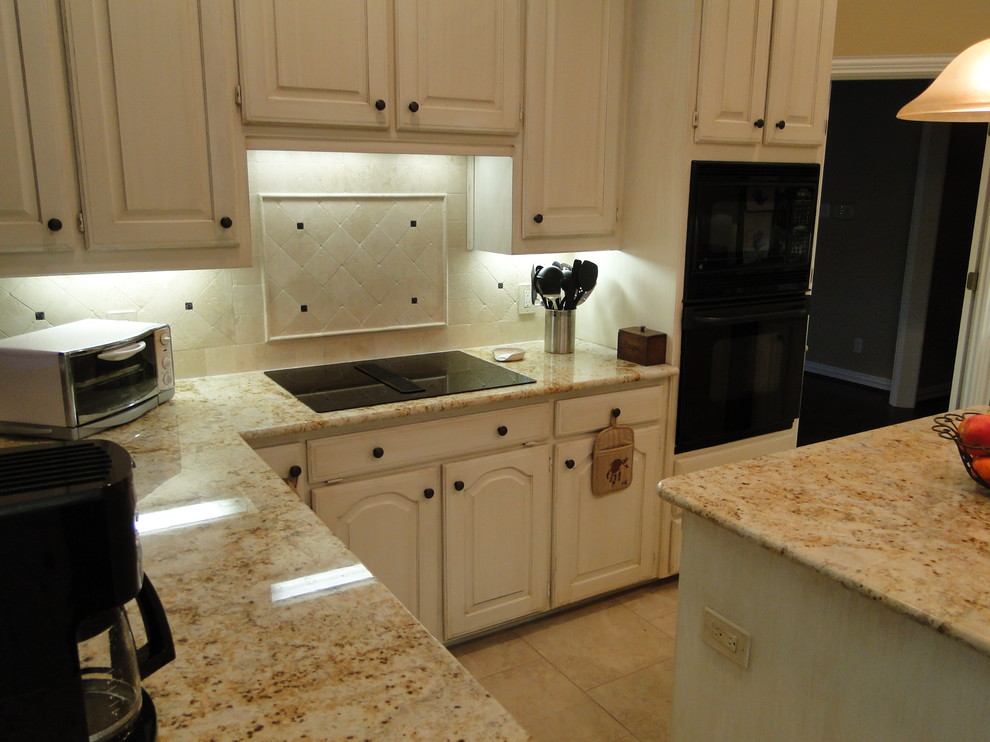 This is an example of a small traditional l-shaped kitchen pantry in Dallas with raised-panel cabinets, beige cabinets, granite worktops, beige splashback, stone tiled splashback, black appliances, travertine flooring, an island and beige floors.