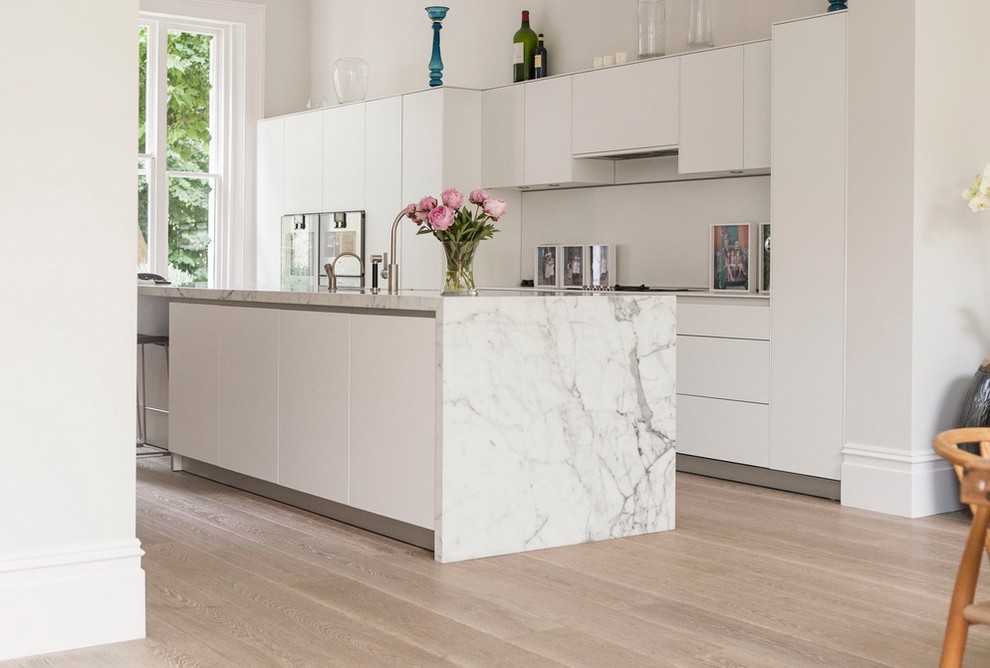 This is an example of a large scandi single-wall kitchen/diner in New York with flat-panel cabinets, white cabinets, marble worktops, light hardwood flooring, an island and beige floors.