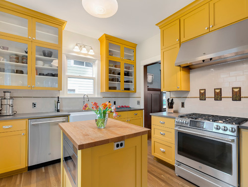 Kitchen and Bathroom Cabinets: yellow shaker kitchen with glass-front uppers, farmhouse sink, stainless range, subway tile, and butcher-block island.