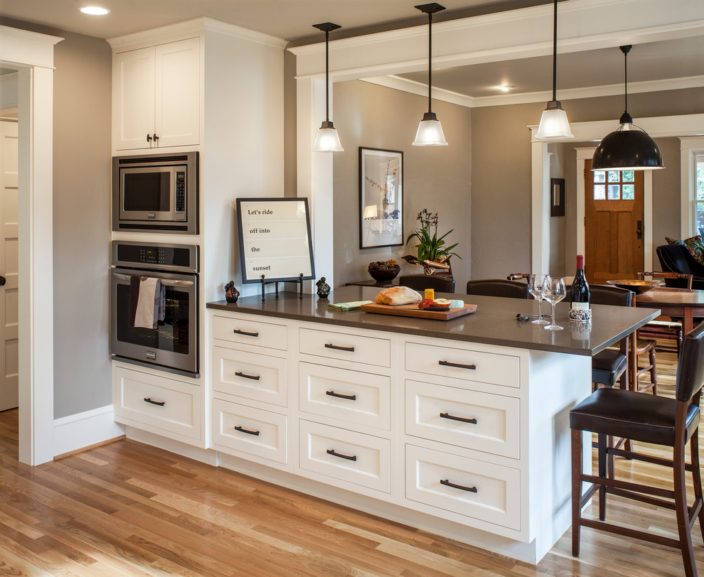 Medium sized classic u-shaped open plan kitchen in Portland with a submerged sink, shaker cabinets, white cabinets, engineered stone countertops, stainless steel appliances, light hardwood flooring and a breakfast bar.