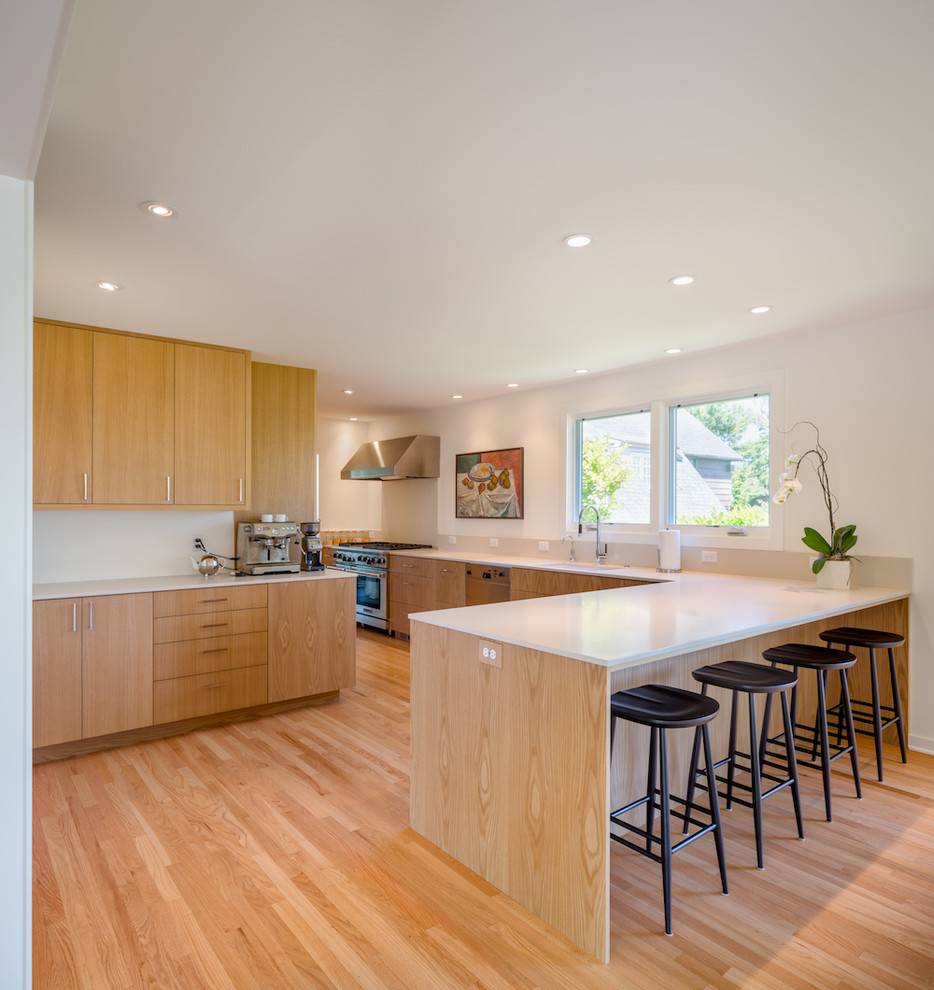 Modern inredning av ett kök med öppen planlösning, med släta luckor, skåp i mellenmörkt trä, grått stänkskydd, rostfria vitvaror, mellanmörkt trägolv, en halv köksö och brunt golv