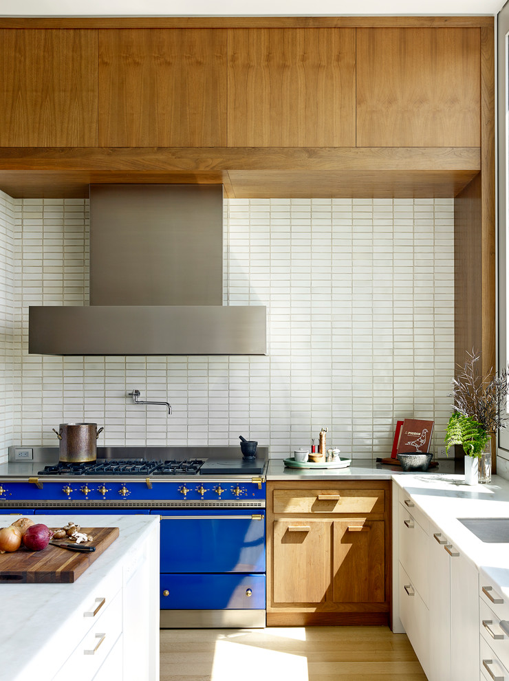 Moderne Küche in L-Form mit Unterbauwaschbecken, flächenbündigen Schrankfronten, hellbraunen Holzschränken, Küchenrückwand in Weiß, bunten Elektrogeräten, hellem Holzboden, Kücheninsel, beigem Boden und weißer Arbeitsplatte in Portland