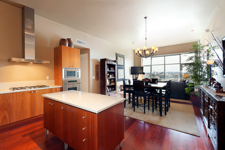 Example of a small asian l-shaped dark wood floor and red floor eat-in kitchen design in Portland with flat-panel cabinets, medium tone wood cabinets, solid surface countertops, white backsplash, stainless steel appliances and an island