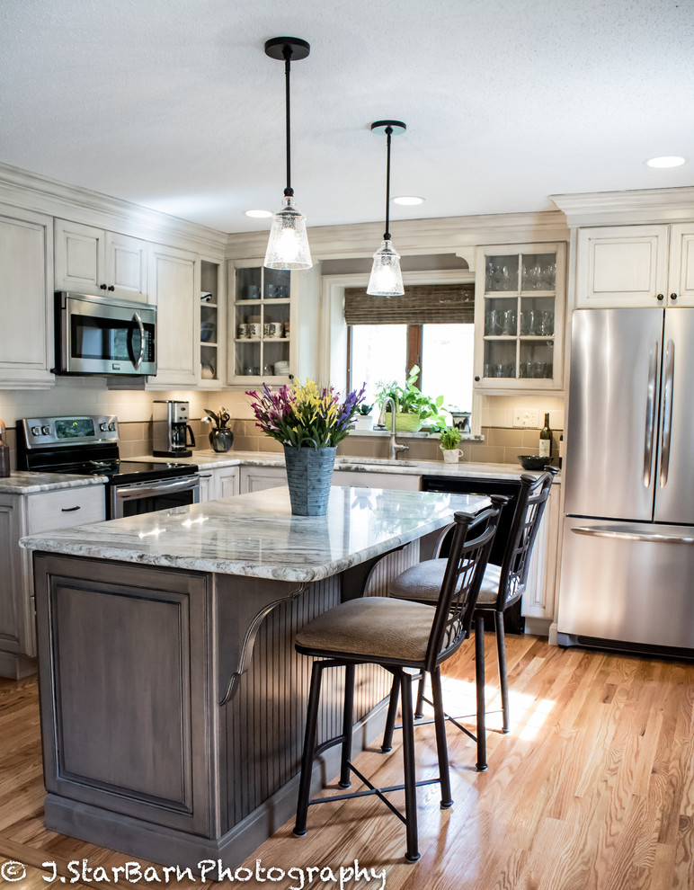 Eat-in kitchen - mid-sized traditional l-shaped medium tone wood floor eat-in kitchen idea in New York with an undermount sink, raised-panel cabinets, yellow cabinets, granite countertops, beige backsplash, porcelain backsplash, stainless steel appliances and an island