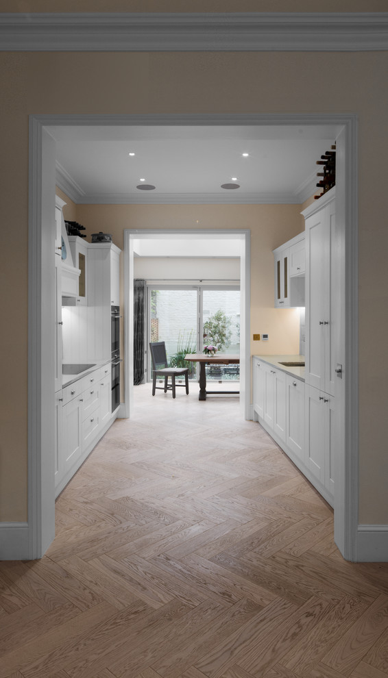 Medium sized traditional galley kitchen pantry in London with a submerged sink, shaker cabinets, white cabinets, limestone worktops, limestone splashback, integrated appliances, medium hardwood flooring, no island and brown floors.