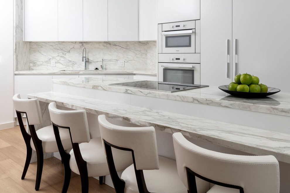 Inspiration for a large contemporary u-shaped medium tone wood floor and brown floor eat-in kitchen remodel in Miami with an undermount sink, flat-panel cabinets, white cabinets, marble countertops, white backsplash, marble backsplash, paneled appliances, an island and white countertops